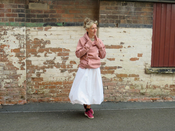 Female model wearing the pink wild isle clothing hoodie with white skirt and pink trainers 