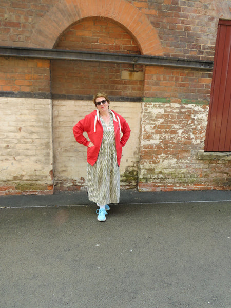 Person wearing a red Wild Isle Trail Zip Up Hoodie and patterned dress standing in front of a brick wall.