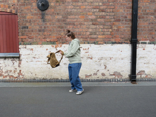 Model putting the waxed canvas roll top back pack on 