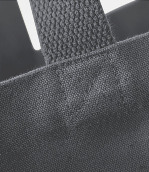Close-up detail of a dark gray woven fabric tote bag showing the texture of the canvas body and a thick woven handle attachment.