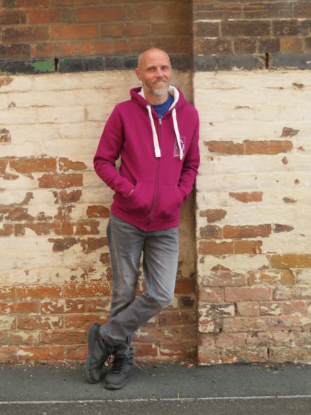 Person wearing a Wild Isle Trail Zip Up Hoodie standing on a pavement with a brick wall behind.