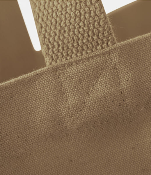 Close-up detail of a sand canvas tote bag showing the woven strap attachment and fabric texture.