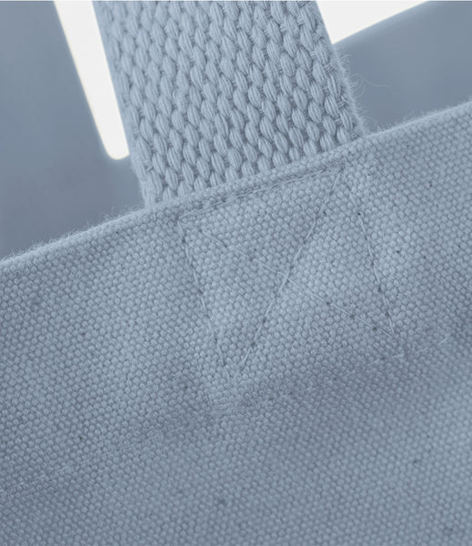 Close-up detail of a light blue canvas tote bag showing the woven strap attachment and fabric texture.