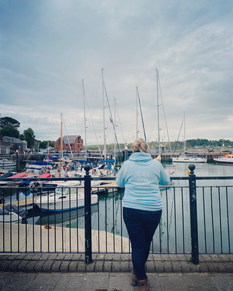 Sarah Pennell wearing the light blue wild isle hoodie at Padstow harbour