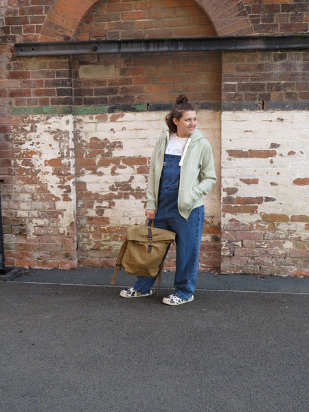 Person wearing the Wild Isle Zip Up Hoodie in Sea Foam, holding the Waxed Canvas Roll Top Bag in Sand colour.