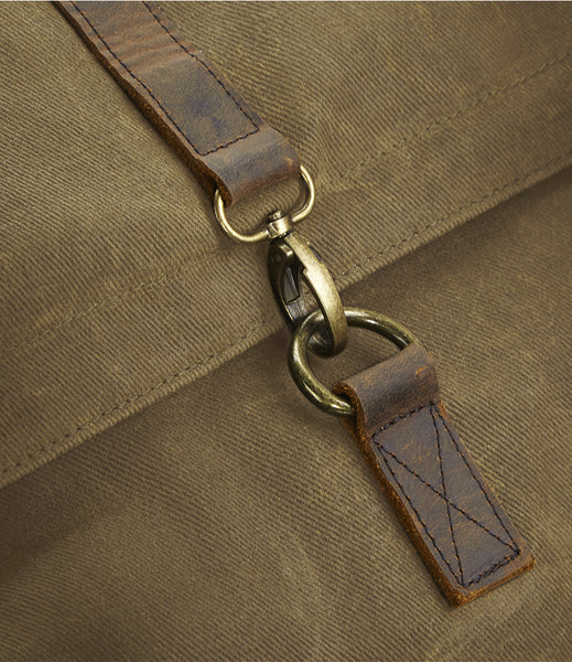Close-up of a brown leather strap attached to a sand canvas bag with brass-tone metal rings and swivel hardware.