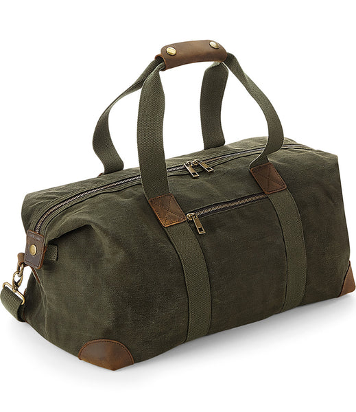 A moss green Wild Isle cabin bag with leather trim and brass effect fittings, featuring two handles and a detachable shoulder strap.