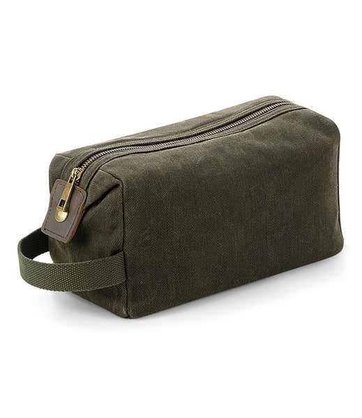 A moss green waxed canvas wash bag with a zippered main compartment and a cotton webbing grab handle.