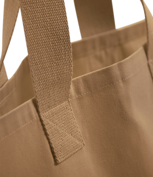 Close-up of a sand canvas tote bag showing the woven fabric texture and a thick webbed handle against a white background.