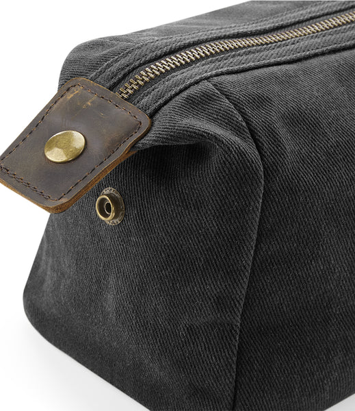 Close-up of the wild isle waxed canvas wash bag with a brown leather strap and brass snap closure, set against a plain white background.