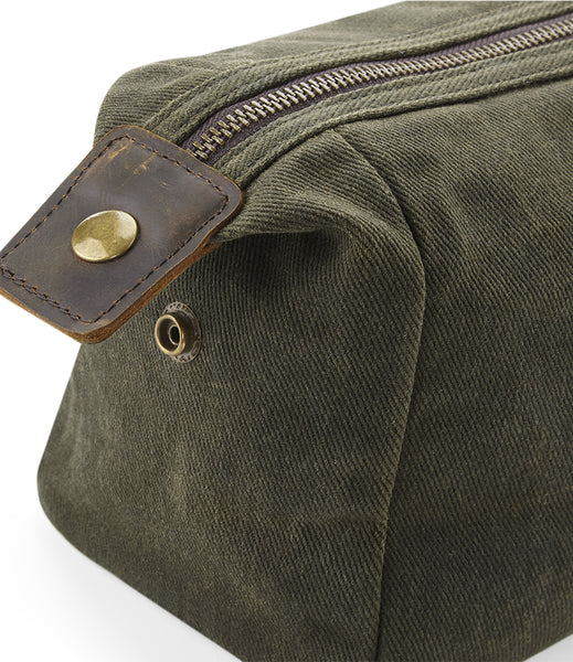 Close-up of the wild isle moss green waxed canvas wash bag with a brown leather tab and brass snap closure, set against a plain white background.