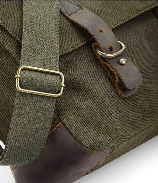Close-up of the wild isle waxed canvas bag with leather accents and brass buckles on a white background