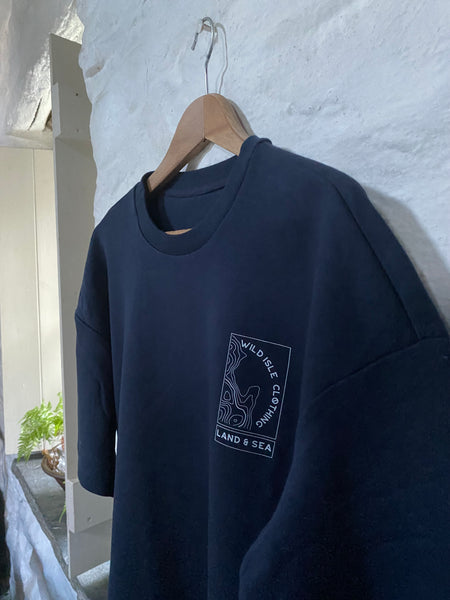 The Wild Isle Terry T-shirt hanging on a hook on a white wash wall.