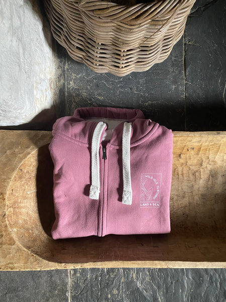 Folded pink hoodie with white drawstrings on a wooden surface next to a woven basket.