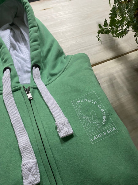 Wild Isle Trail Zip Up Hoodie in Grass Green on a table 