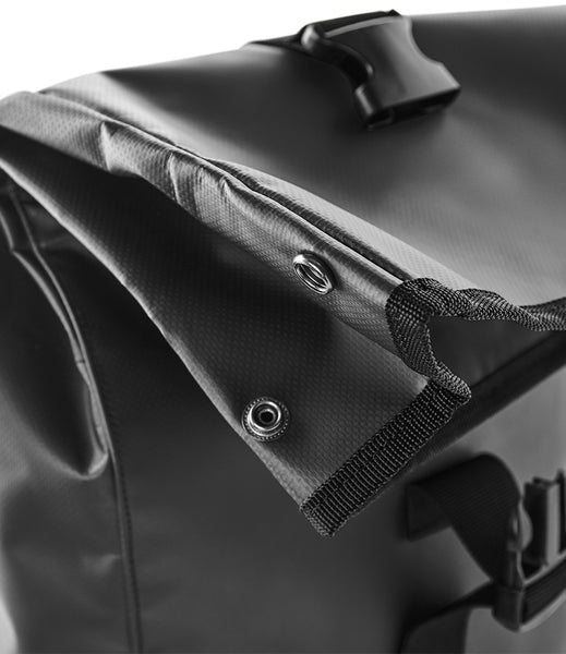 Close-up of a black waterproof roll-top bag showing the textured fabric, metal grommets, and black strap with plastic buckle.