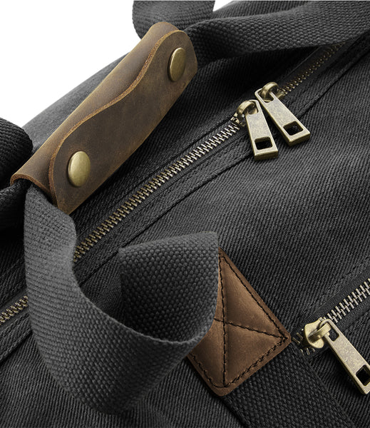 Close-up of a wild isle black cabin bag with brown leather straps and brass zippers.