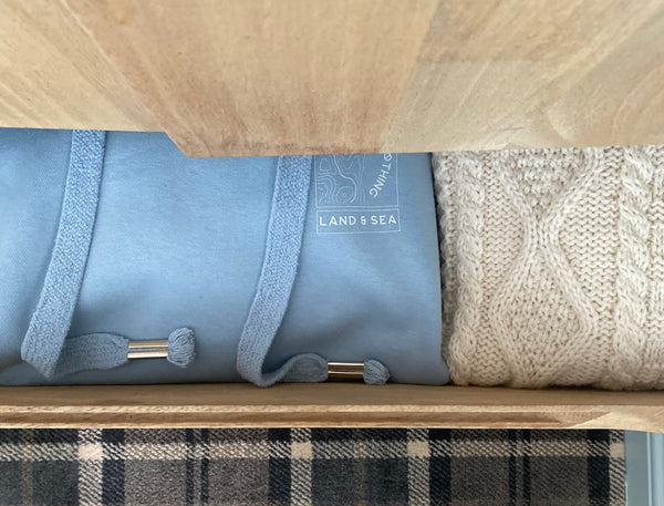 Folded light blue wild isle hoodie and British knitwear Aran jumper in a drawer 