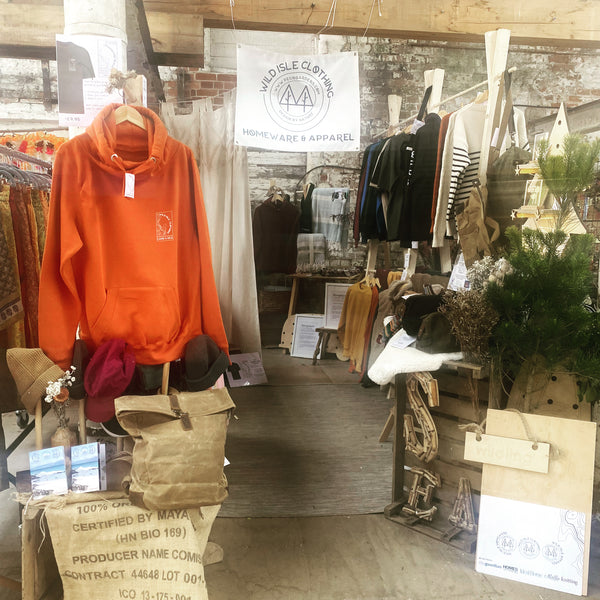 The wild isle clothing pop up shop showing hoodies knitwear and waxed canvas bags with a wood aesthetic